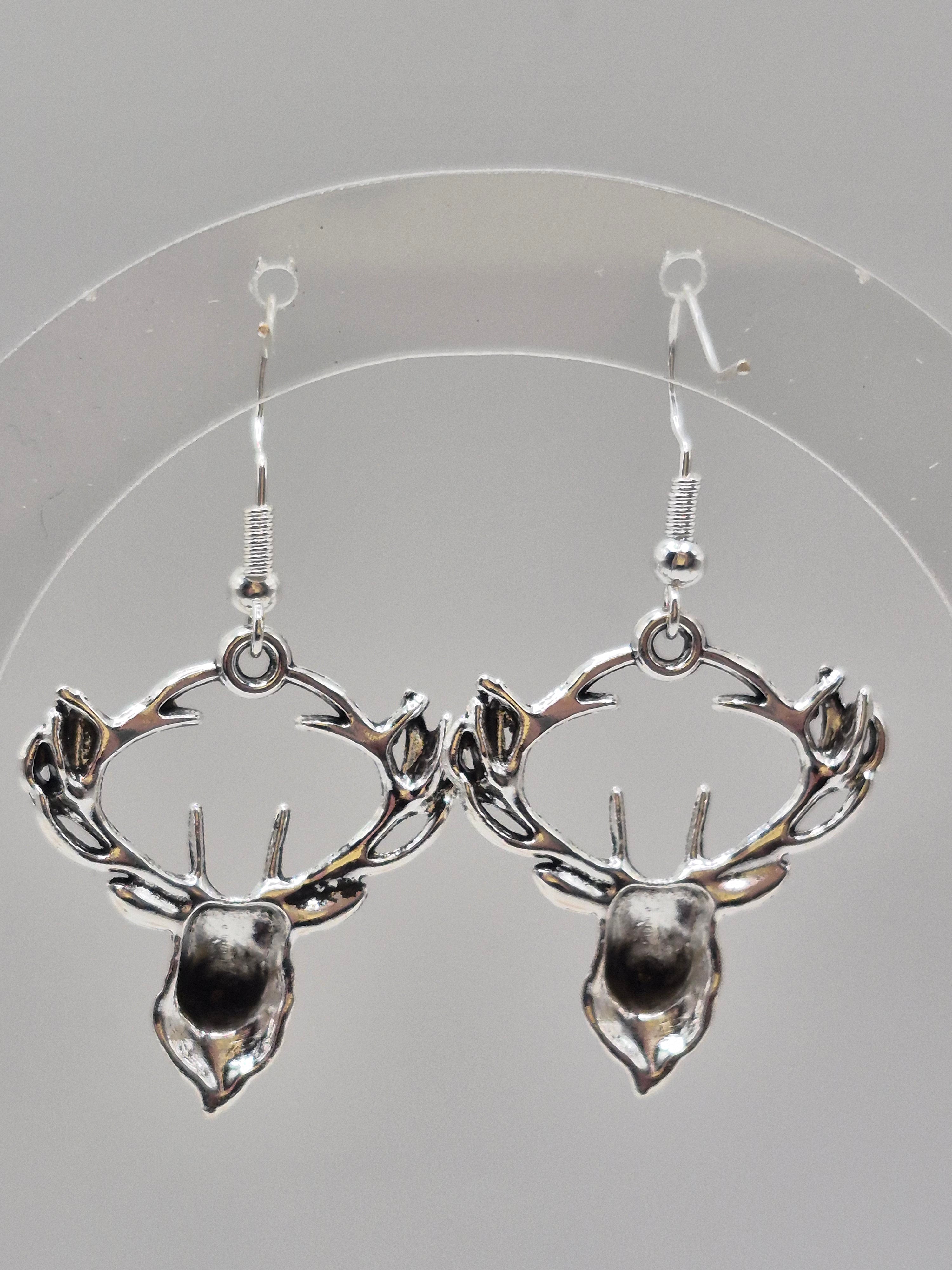 A pair of silver-toned dangle earrings with a stylized leaf and branch design, displayed on a clear circular stand against a light gray background.